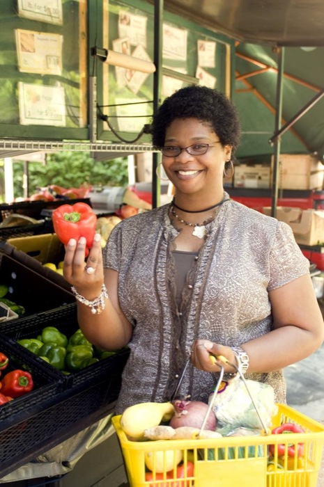 With her shopping basket filled with an array of healthy food choices, this woman had completed her selection process at a mobile produce market, and was shown holding up a bright red bell pepper. Some of the vegetables she’d placed into her basket included a lemon, a head of cauliflower, a purple and a white onion, ginger root, and a variety of bell peppers.